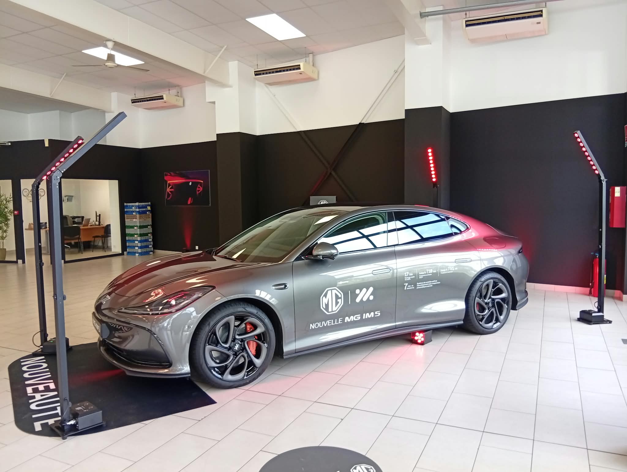 Présentation d'un véhicule MG en concession automobile mis en valeur par un éclairage LED rouge sur mâts autonomes.